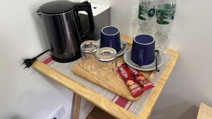 Una cuineta petita amb una cafetera, dues tasses, dos vasos i dues ampolles d'aigua sobre una taula de fusta.