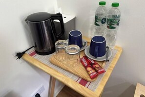 A small kitchenette with a coffee maker, two cups, two glasses, and two water bottles on a wooden table.