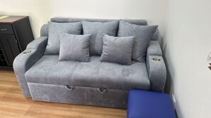 Un sofà gris amb reposabracs i un otomà blau en una habitació amb sòls de fusta.