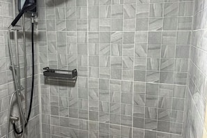 Un área de ducha con pared de azulejos, cabezal de ducha manual y grifo empotrado.