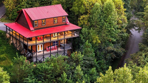 Une cabane en bois à deux étages, avec un toit rouge, entourée d’une forêt dense et d’une rivière.
