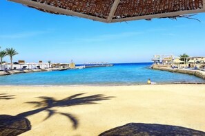 A beach with a clear sky, a sandy shore, and a structure with a roof overlooking the water. - New Geisum Resort (Hurghada)