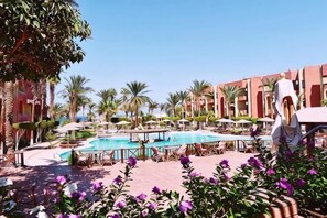 A pool area with multiple pools, palm trees, and a building with balconies. - New Geisum Resort (Hurghada)