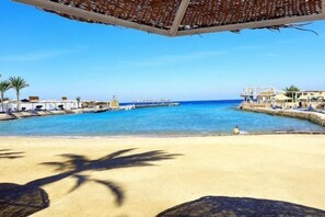 A beach with a clear blue sky, a sandy shore, and a structure with a roof overlooking the water. - New Geisum Resort (Hurghada)