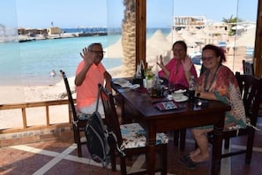 Une table à manger avec des chaises, une vue sur la plage et un palmier.