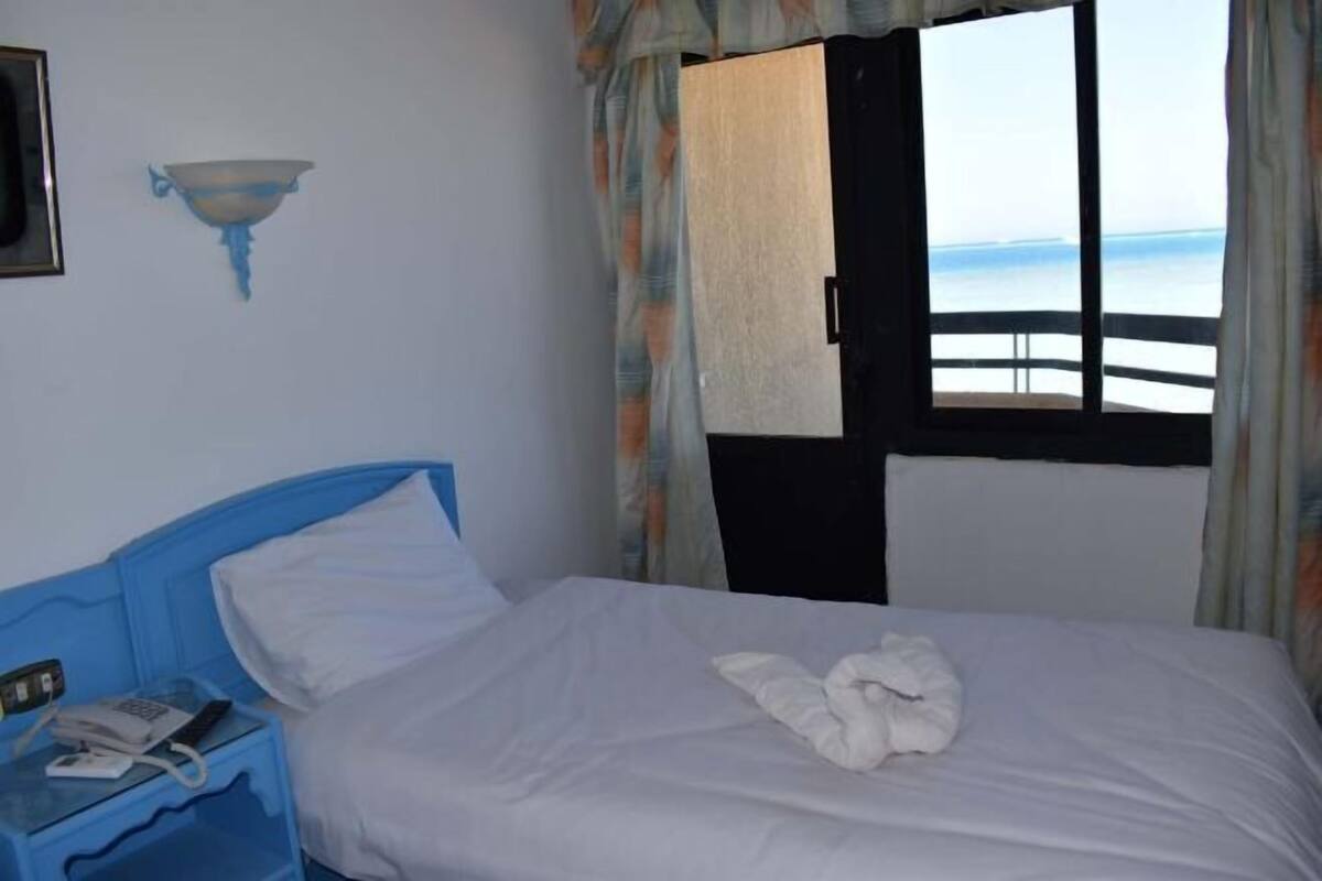 Une chambre d’hôtel avec un lit, un téléphone sur la table de chevet, une fenêtre avec des rideaux et une vue sur la mer.