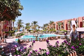 A resort pool area with multiple pools, palm trees, and a building with balconies. - New Geisum Resort (Hurghada)