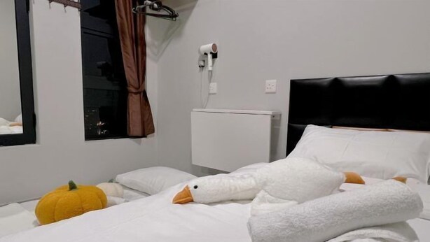 A hotel room with a bed, a white duck-shaped pillow, a yellow pumpkin decoration, a white radiator, and a black headboard. - JQ Angel (Little Angel B&B) New/CitySeaview/LV29/Netflix/6pax (Kota Kinabalu)