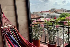 Een balkon met een hangmat, plantenpotten en uitzicht op gebouwen.