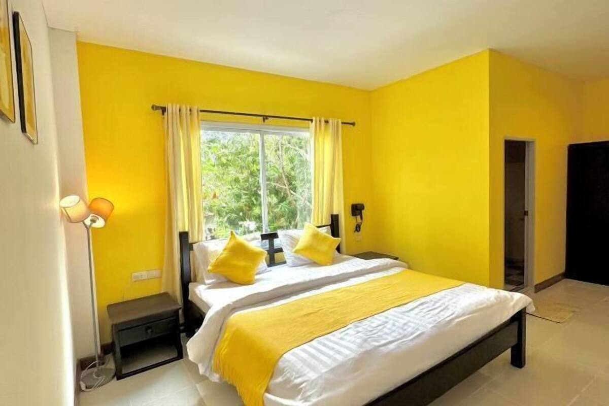 Una habitación con una cama, una mesita de noche, una lámpara y una ventana con cortinas.