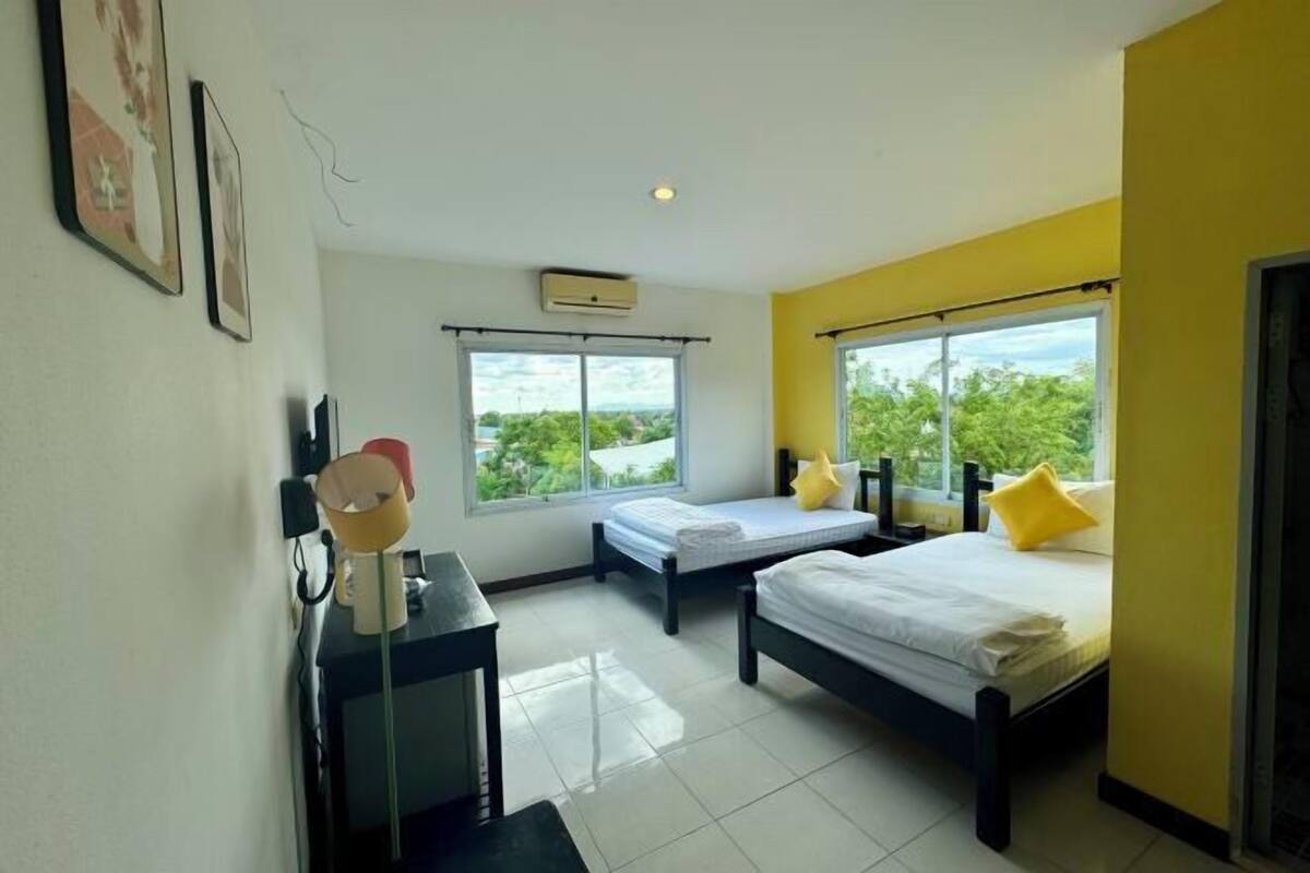 Habitación de hotel con dos camas, un escritorio, una silla, un ventanal con vistas y un equipo de aire acondicionado.