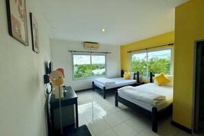 A hotel room with two beds, a desk, a chair, a window with a view, and an air conditioning unit. - KK Hotel Pakse (Pakse)