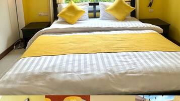 Habitación de hotel con cama, almohadones amarillos, mesita de noche y ventana con vistas a follaje.