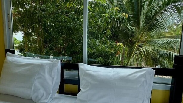 A bed with white pillows and striped bedding, a window with a view of palm trees. - KK Hotel Pakse (Pakse)