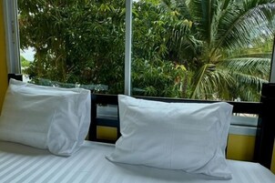 A bed with white pillows and striped bedding, a window with a view of palm trees.