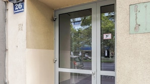 A building entrance with a glass door, a street sign indicating '26', and a 'No Parking' sign.