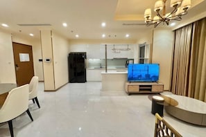 A modern living room with a dining area, a kitchen in the background, and a TV on a stand. - Vinhomes Chic Apartment - Ho Chi Minh (Ho Chi Minh City)