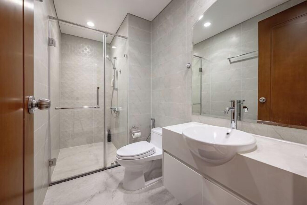Ein modernes Badezimmer mit Duschkabine aus Glas, Toilette in Weiß und großem Waschbecken mit Spiegel.