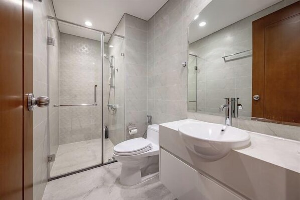Ein modernes Badezimmer mit Duschkabine aus Glas, Toilette in Weiß und großem Waschbecken mit Spiegel.