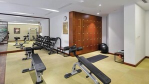 Ein Fitnessstudio mit Trainingsgeräten, Bänken, einer Spiegelwand und einem Holzumkleidebereich.