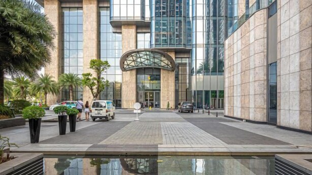 A modern building with a glass facade, a central entrance with a curved canopy, and a reflective water feature in the foreground. - Vinhomes Chic Apartment - Ho Chi Minh (Ho Chi Minh City)