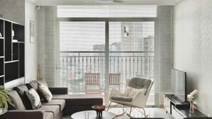 A modern living room with a sofa, armchair, and coffee table, large windows with blinds, and a ceiling fan. - Vinhomes Chic Apartment - Ho Chi Minh (Ho Chi Minh City)