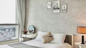 A modern hotel room with a large bed, a nightstand with a lamp, a view of the city through the window, and three framed pictures on the wall. - Vinhomes Chic Apartment - Ho Chi Minh (Ho Chi Minh City)