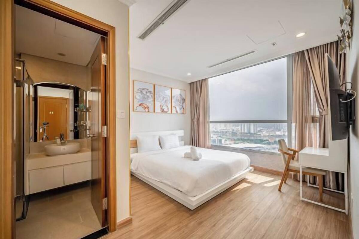 Ein modernes Hotelzimmer mit einem großen Bett, einem Schreibtisch, Blick auf die Stadt und einem Badezimmer mit Waschbecken und Spiegel.