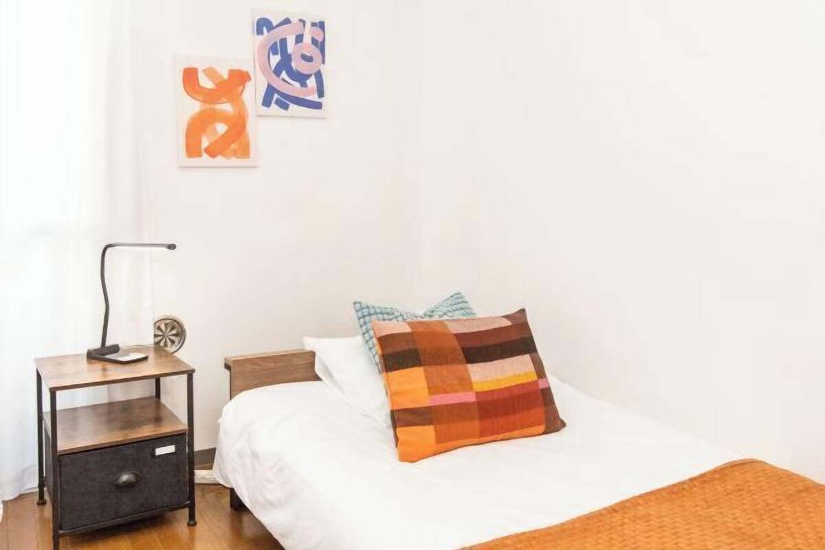 A bedroom with a bed, a nightstand, a lamp, and abstract wall art.