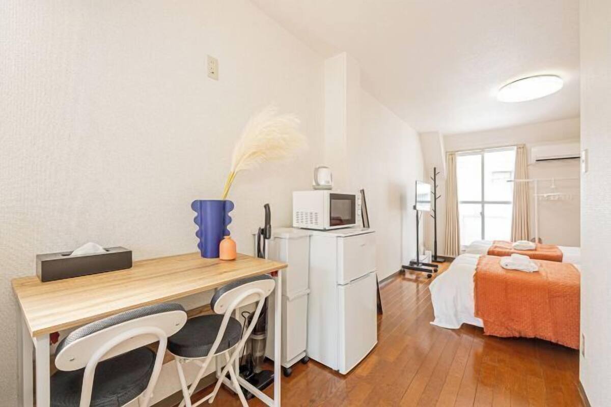 A compact hotel room with a kitchenette, a dining area, and a bed with an orange blanket.