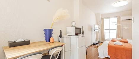 Una habitación de hotel compacta con kitchenette, un área de comedor y una cama con manta naranja.