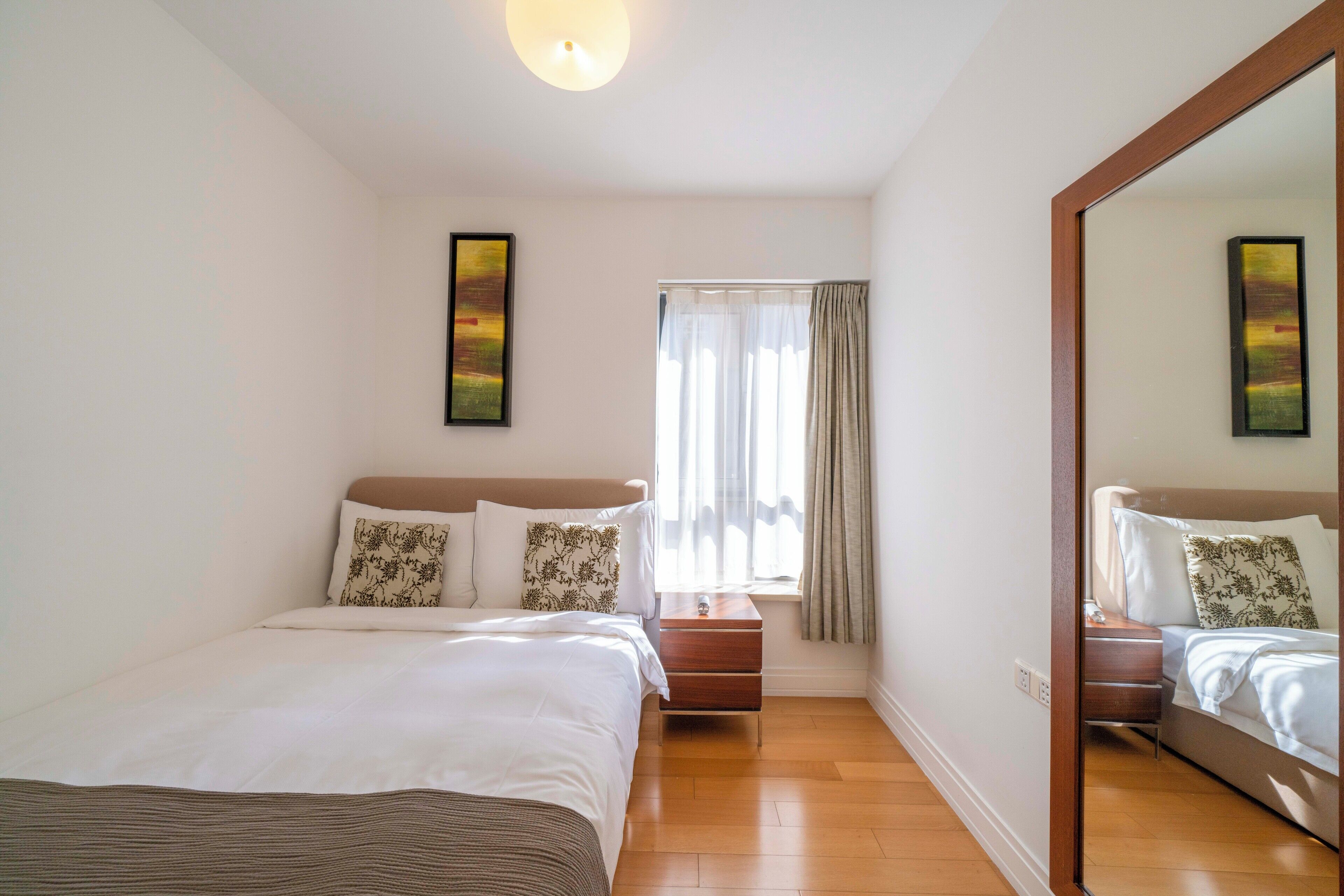 Quarto com uma cama grande, mesa de cabeceira, janela com cortinas e espelho na parede.