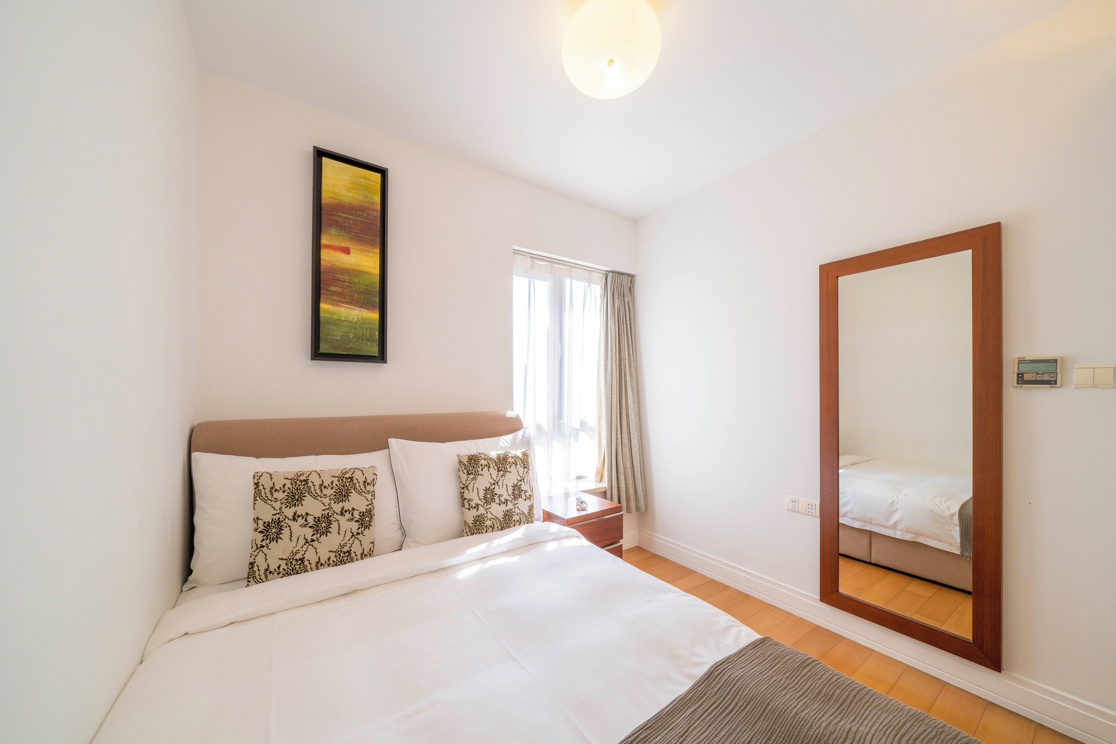 A bedroom with a large bed, a bedside table, a mirror, and a window with curtains.