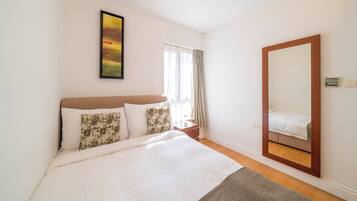 A bedroom with a large bed, a bedside table, a mirror, and a window with curtains.