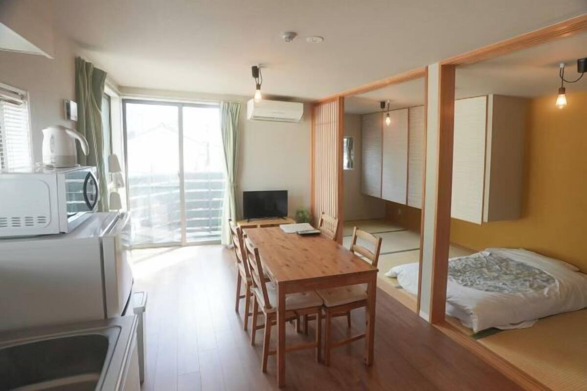 Ett kompakt bostadsutrymme med ett matbord, stolar, en säng, en TV och ett litet kök.