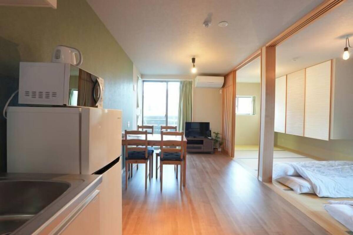 Ett kompakt bostadsutrymme med ett litet kök, en matplats, en tv och en säng.