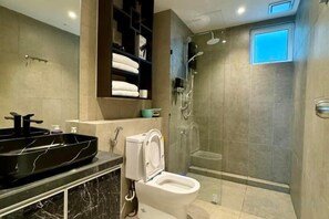 Une salle de bain moderne avec un lavabo noir, des toilettes blanches et une douche séparée par une paroi de verre.