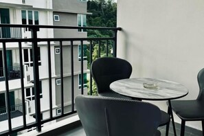 A balcony with a round table and two chairs, overlooking a building and greenery. - Sri Indah Luxury HomeStay (Sandakan)