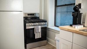 Una cocina con horno de acero inoxidable, cafetera y ventana con persianas.