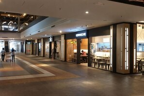 Ein modernes Einkaufszentrum im Inneren, mit einem Café namens 'CUPNICE' und einem Restaurant mit Außenbereich.