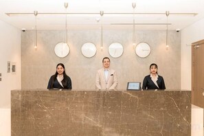 Un comptoir d’accueil avec trois employés, un comptoir en marbre et des horloges murales.