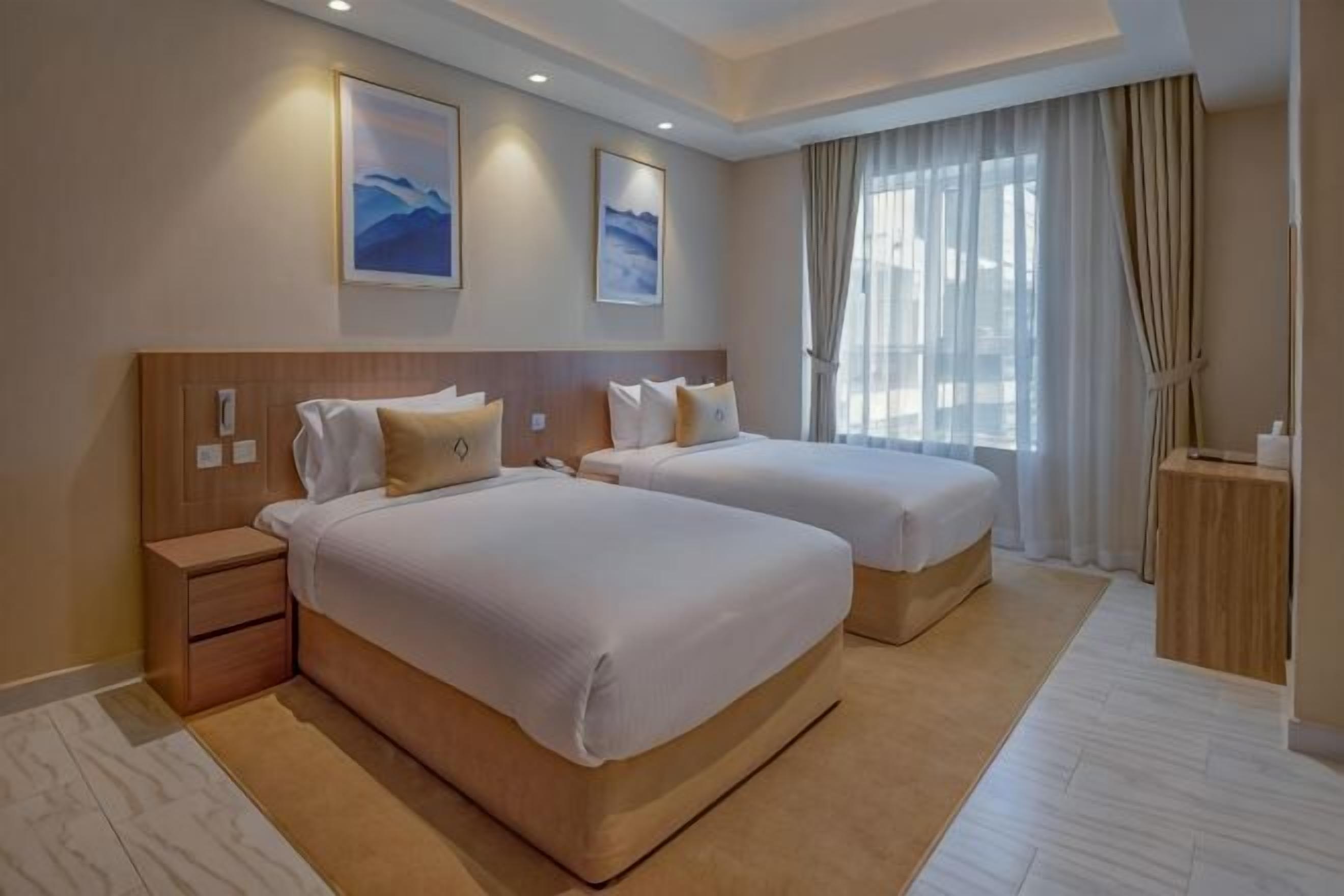 Ein Hotelzimmer mit zwei Betten, einem Nachttisch, einem kleinen Tisch und einem großen Fenster mit Vorhängen.