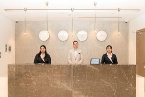 Un comptoir d’accueil avec trois employés, un dessus de comptoir en marbre et des horloges fixées au mur.