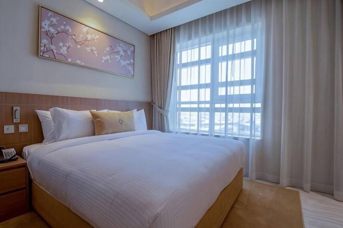 Habitación de hotel con una cama grande, una mesita de noche, un teléfono en la pared y una ventana con cortinas.