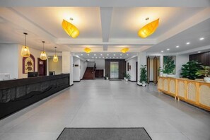 A spacious lobby with a reception desk, modern pendant lighting, and a staircase leading to upper floors.