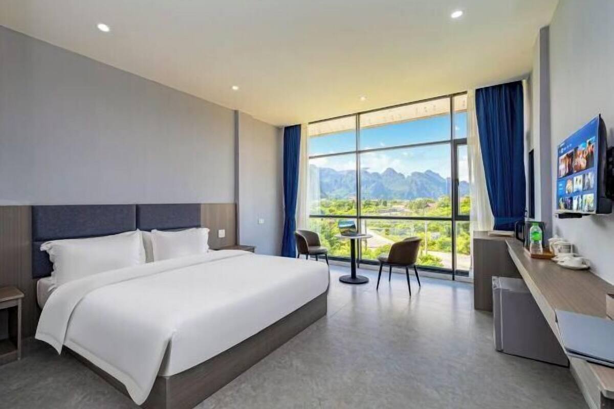 Une chambre d’hôtel avec un grand lit, un bureau, des chaises, un petit réfrigérateur et une fenêtre donnant sur la montagne.