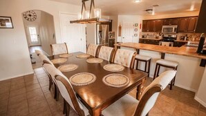 Un comedor con una mesa y sillas de madera, una araña y una cocina al fondo.
