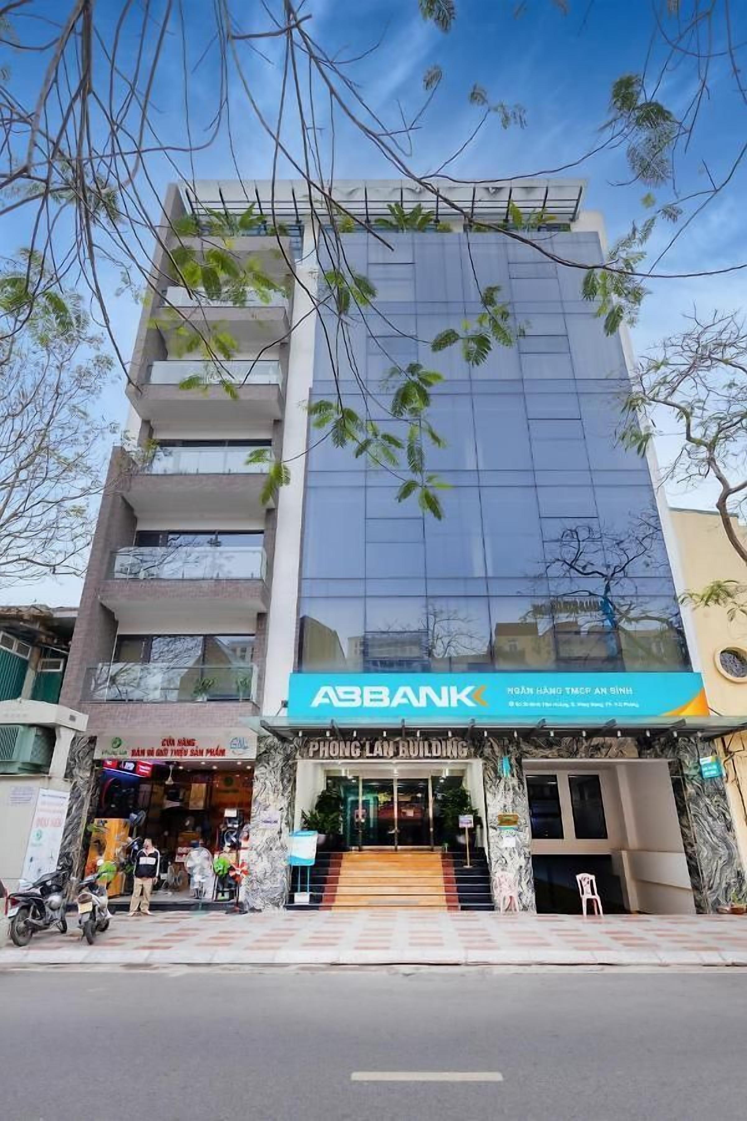 Um edifício com vários andares, fachada de vidro moderna, um letreiro ASBANK bem visível e uma entrada com escadaria que leva ao andar térreo.