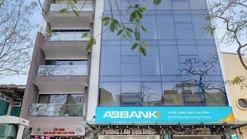 Um edifício com vários andares, fachada de vidro moderna, um letreiro ASBANK bem visível e uma entrada com escadaria que leva ao andar térreo.