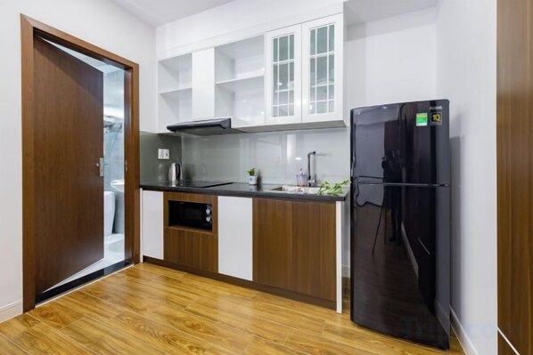 A compact kitchen with a black refrigerator, wooden cabinets, and a white countertop. - Phong Lan Building and Apartments (Haiphong)
